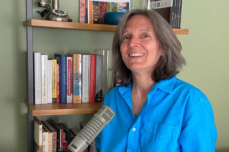 Karen laughing at she sits in front of a bookshelf at a microphone.