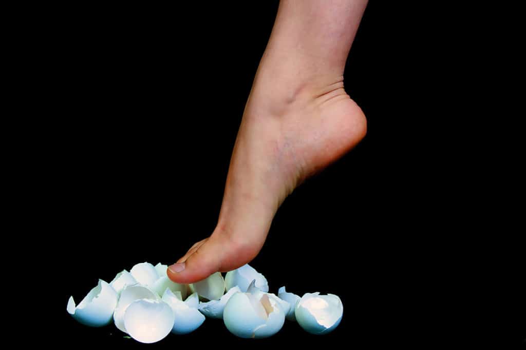 bare foot about to step on eggshells that are broken in half.