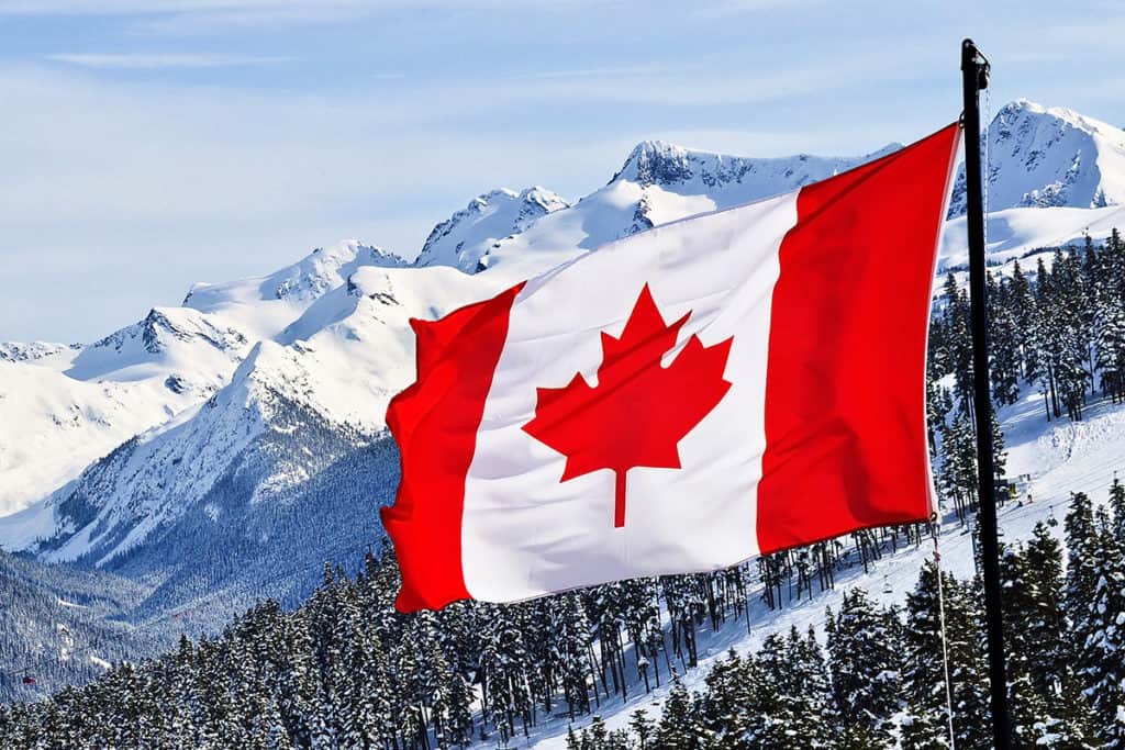 Canadian flag waves in the wind against a backdrop of snowy rocky mountains.