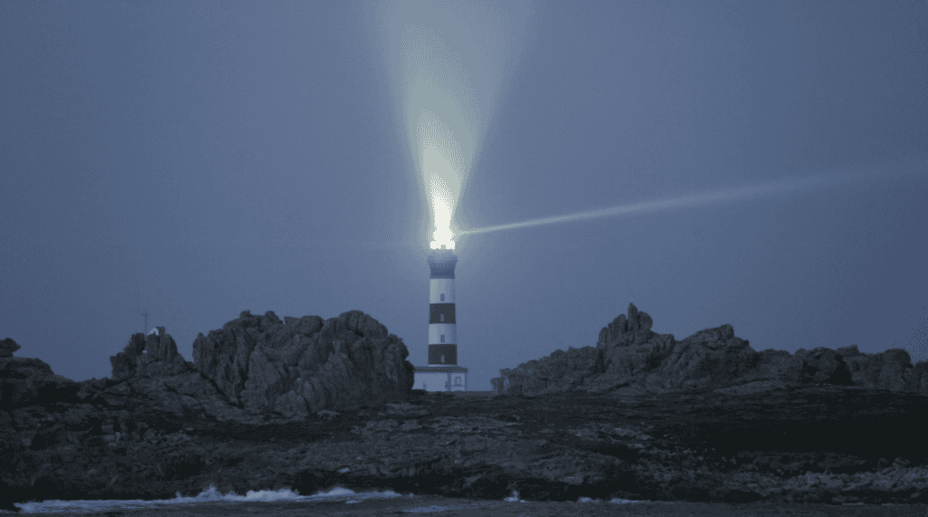 Lighthouse on a rocky coast at dusk with the search light shining bright.